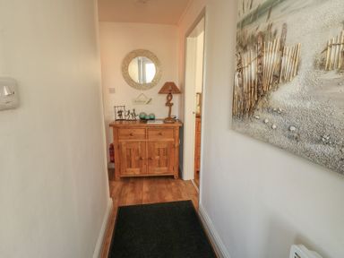 A hallway with a wooden cabinet a round mirror and a lamp a painting on the wall at Camwy in Brynsiencyn