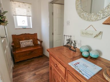 A small hallway with wooden bench with a cushion and wooden sideboard with decorative items at Camwy Brynsiencyn