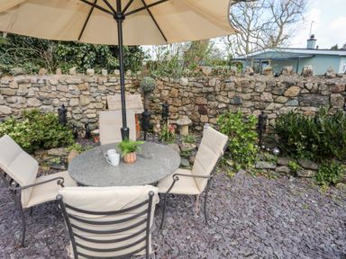 An outdoor patio area with a round table under an umbrella surrounded by four cushioned chairs and a stone wall in the background at Camwy in Brynsiencyn