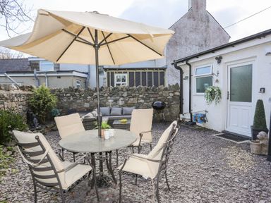 An outdoor patio with a round table and four chairs under an umbrella and a stone wall at Camwy in Brynsiencyn