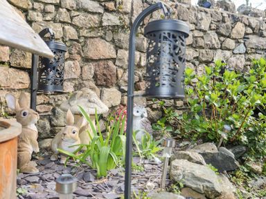 A garden area with stone wall decorated with rabbit and owl statues and black lanterns at Camwy in Brynsiencyn