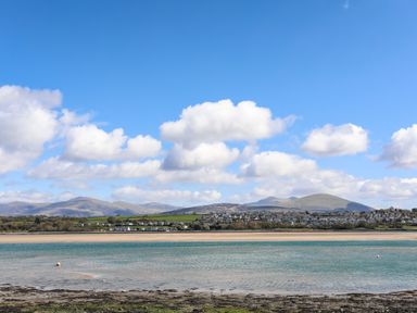 A coastal scene with a sandy beach water hills and houses under a blue sky at Camwy in Brynsiencyn