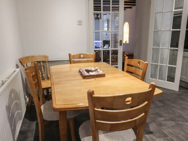 A dining room with a wooden table and five wooden chairs near white walls and glass panel doors at Ty Glyn in Beddgelert
