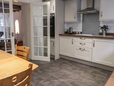 A kitchen with wooden dining table and chairs white cabinets and tiled floor at Ty Glyn in Beddgelert