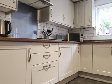 A kitchen with white cabinets wooden countertop microwave kettle and utensils at Ty Glyn in Beddgelert