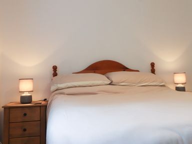 A bed with beige bedding and two lamps on wooden bedside tables at Ty Glyn in Beddgelert