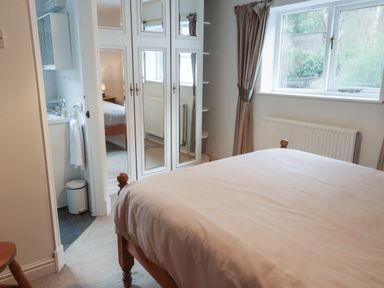 A bedroom with a wooden bed near a window and mirrored wardrobe doors at Ty Glyn in Beddgelert