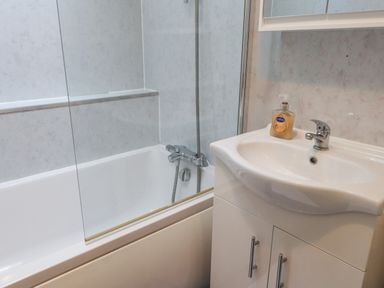 A bathroom with a bathtub shower and a sink with soap dispenser at Ty Glyn in Beddgelert