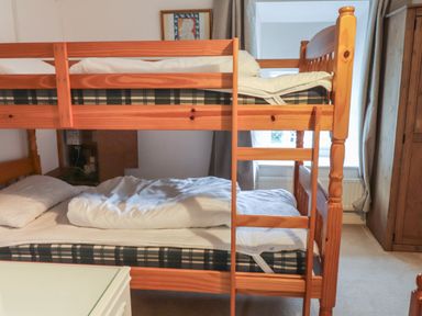 A wooden bunk bed with pillows and bedding in a bedroom with a window and wooden wardrobe at Ty Glyn in Beddgelert