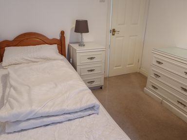 A bedroom with a wooden bed white bedding white bedside table with a lamp white chest of drawers and a closed door at Ty Glyn in Beddgelert