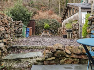 An outdoor patio area with stone walls a wooden bench several plant pots recycling bins and a small shed at Ty Glyn in Beddgelert