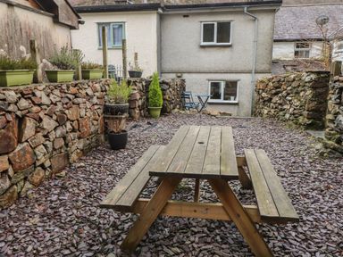 An outdoor patio area with a wooden picnic table surrounded by stone walls and potted plants at Ty Glyn in Beddgelert
