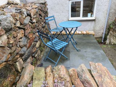 An outdoor patio area with a blue metal table and two matching chairs surrounded by stone walls at Ty Glyn in Beddgelert