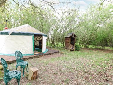 A yurt with two green chairs and wood storage in a wooded area at Brandon House Farm Yurt Brandon Parva near Mattishall