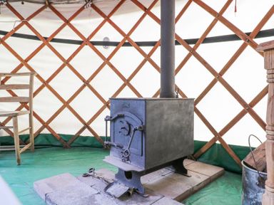 A wood burning stove inside a yurt with a wooden chair and wood bucket at Brandon House Farm Yurt Brandon Parva near Mattishall