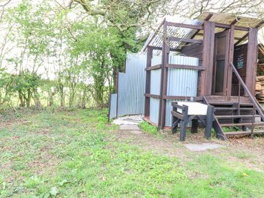 An outdoor shower and washbasin area with metal panels and wooden structure surrounded by trees at Brandon House Farm Yurt in Brandon Parva near Mattishall