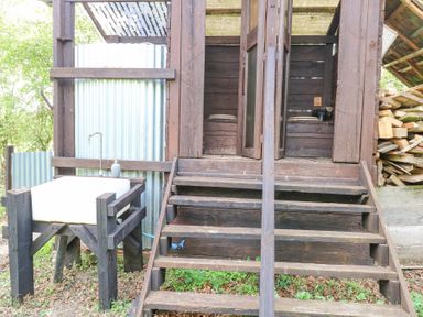 An outdoor wooden structure with steps leading to two doors and a white sink on a wooden stand at Brandon House Farm Yurt Brandon Parva near Mattishall