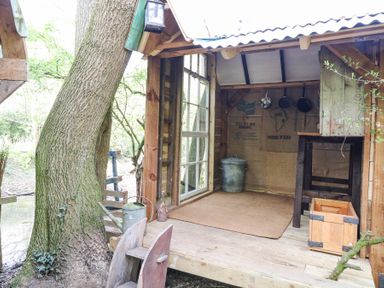 A small wooden outdoor shed with an open door showing hanging pans a metal bucket a wooden crate and a watering can at Brandon House Farm Yurt Brandon Parva near Mattishall