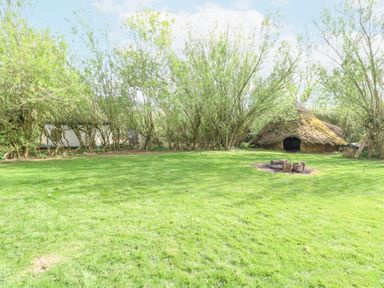 An outdoor area with grass fire pit trees wooden hut and yurt at Brandon House Farm Yurt Brandon Parva near Mattishall