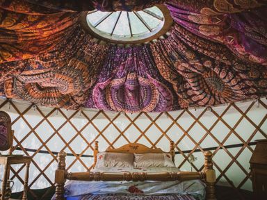 A wooden bed with pillows and bedding under a colorful fabric ceiling in a yurt at Brandon House Farm Yurt Brandon Parva near Mattishall