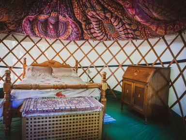 A wooden bed with a patterned cover and a wooden chest at the foot inside a yurt with patterned fabric on the ceiling and a wooden cabinet Brandon House Farm Yurt Brandon Parva near Mattishall