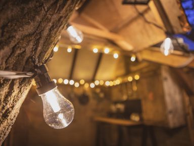 A close up of a string light bulb attached to a tree with more string lights blurred in the background at Brandon House Farm Yurt Brandon Parva near Mattishall