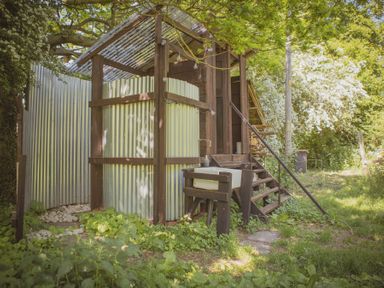 An outdoor rustic shower area with corrugated metal panels a wooden sink and steps leading to a small cabin at Brandon House Farm Yurt Brandon Parva near Mattishall