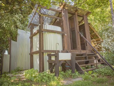 An outdoor wooden structure with corrugated metal walls a sink a small staircase and surrounding greenery at Brandon House Farm Yurt Brandon Parva near Mattishall