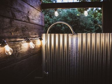 An outdoor shower with a metal corrugated wall wooden wall with string lights hanging at Brandon House Farm Yurt Brandon Parva near Mattishall