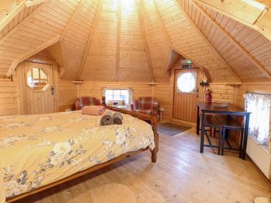 A wooden interior bedroom with a bed with floral bedding two armchairs a table with benches and wooden walls at Enchanted Cottage in Snettisham