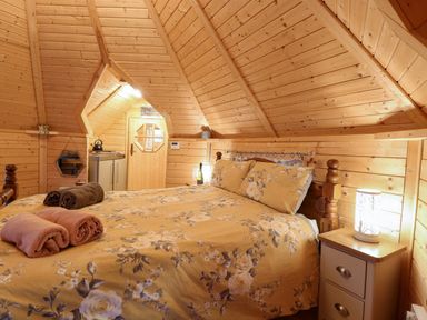 A bedroom with a floral bedspread and rolled towels on the bed in a wooden cabin at Enchanted Cottage in Snettisham