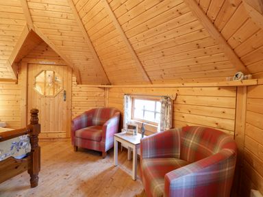 A wooden room with two plaid armchairs a small white table and a window at Enchanted Cottage in Snettisham