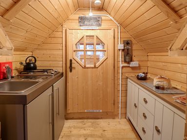 A small wooden kitchen with a sink stove and kettle on the left and cabinets with bread and jars on the right at Enchanted Cottage in Snettisham