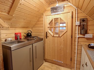 A small wooden kitchen with a sink stove kettle and a door with window at Enchanted Cottage in Snettisham