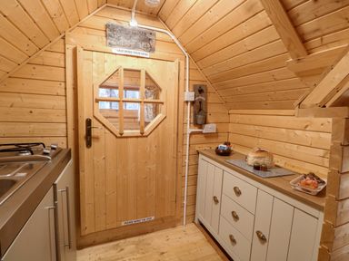 A small wooden kitchen area with a door featuring a window and a cabinet with food items on top at Enchanted Cottage in Snettisham