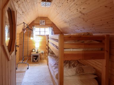 A small wooden bedroom with bunk beds a white rug a standing clothes rack a small table with a lamp and an alarm clock at Enchanted Cottage in Snettisham