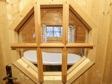A wooden bathroom with a white freestanding bathtub visible through an octagonal window at Enchanted Cottage in Snettisham