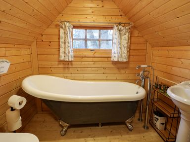 A bathroom with a clawfoot bathtub a small window with curtains wooden walls and floor at Enchanted Cottage in Snettisham