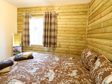 A bedroom with a bed covered in animal print bedding a window with plaid curtains and a standing mirror at Rabbit Warren Lodge in Snettisham