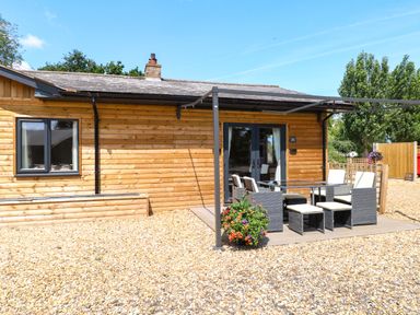 A house with patio furniture and flowers at Rabbit Warren Lodge in Snettisham