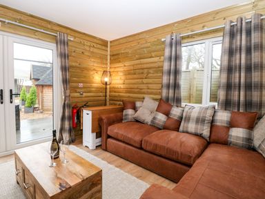 A living room with a brown sectional sofa with plaid cushions near wood paneled walls at Robins Nest Lodge in Snettisham