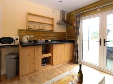 A kitchen area with wooden cabinets microwave kettle sink and sliding glass doors at Robins Nest Lodge in Snettisham