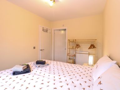 A bedroom with a bed with bird patterned bedding towels on the bed a clothes rack with hangers and baskets and two white doors at Robins Nest Lodge in Snettisham