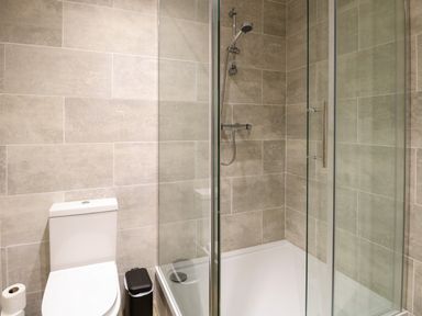 A bathroom with a toilet a trash bin a shower with glass doors and tiled walls at Robins Nest Lodge in Snettisham