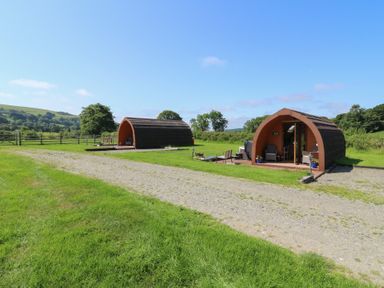 Two glamping pods with patio chairs and grass area at Ty Twt Teifi in Tregaron