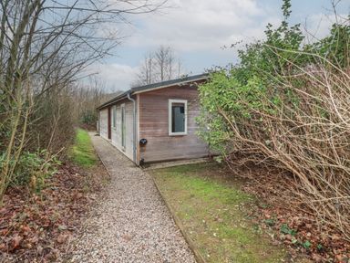 A wooden cabin with a gravel path and surrounding bushes near Lanreath