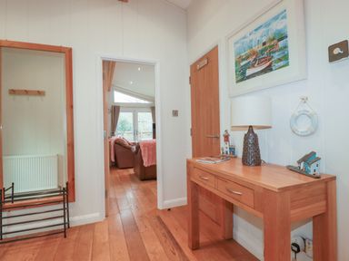 A hallway with wooden floor a large mirror a wooden table with a lamp and decorations a door and a view into a living room at 1 Miller's Island near Lanreath