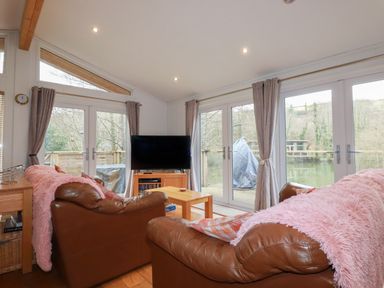 A living room with brown leather sofas pink throws a wooden coffee table and a TV by glass doors at 1 Millers Island near Lanreath