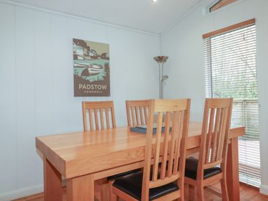 A dining room with a wooden table and four chairs next to a window with blinds at 1 Miller's Island near Lanreath