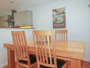 A dining area with a wooden table and chairs with a kitchen in the background at 1 Millers Island near Lanreath